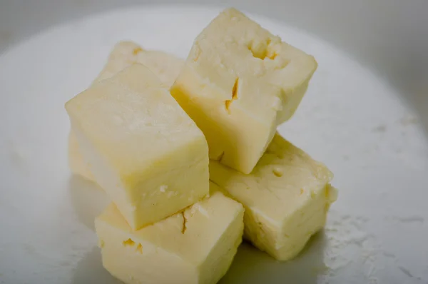 Stajni zbliżenie świeży ser pokroić w kwadratowe kawałki na białej powierzchni — Zdjęcie stockowe
