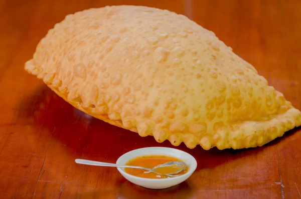 Large fluffy empanada beautiful color lying on wooden surface next to small bowl of salsa — Stock Photo, Image