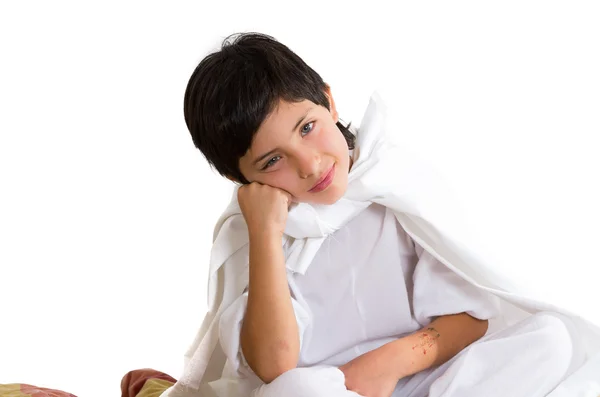 Small boy wearing all white sitting on quilt fabrics leaning head onto fists, thoughtful concept — Stock Photo, Image