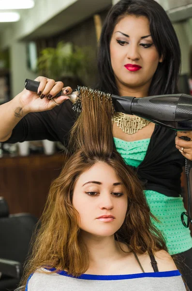 Brunette facing camera getting hair done by professional stylist — стокове фото