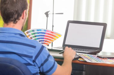 Man working on laptop while holding up pantone palette, colormap from behind angle
