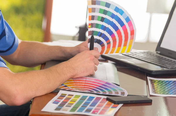 Mãos masculinas segurando paleta pantone, colormap espalhados na frente do laptop na mesa de trabalho — Fotografia de Stock