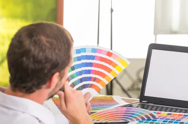 Man working on laptop while holding up pantone palette, colormap from behind angle — Stock Fotó