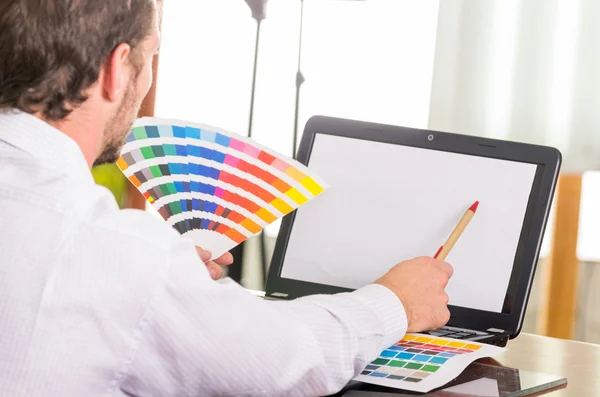 Man working on laptop while holding up pantone palette, colormap from behind angle — Stok fotoğraf