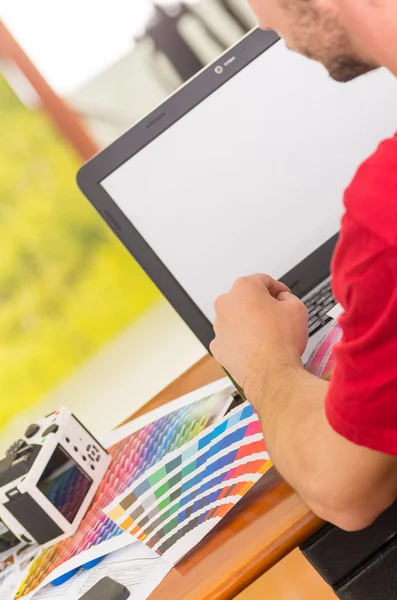 Homem trabalhando no laptop com paleta de pantone, colormap espalhado ao lado dele — Fotografia de Stock