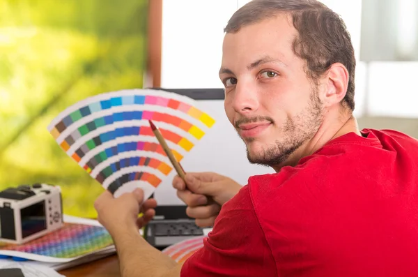 Man working on laptop while holding up pantone palette, colormap from behind angle — ストック写真