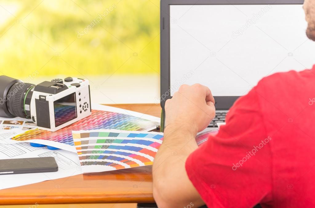 Man working on laptop with camera and pantone palette, colormap spread out next to it