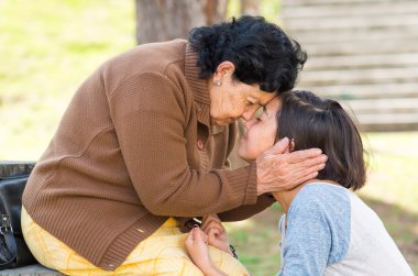 Grandmother facing granddaughter touching heads outdoors, lovely picture displaying love between people clipart