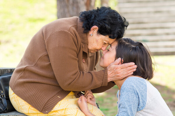 Grandmother facing granddaughter touching heads outdoors, lovely picture displaying love between people
