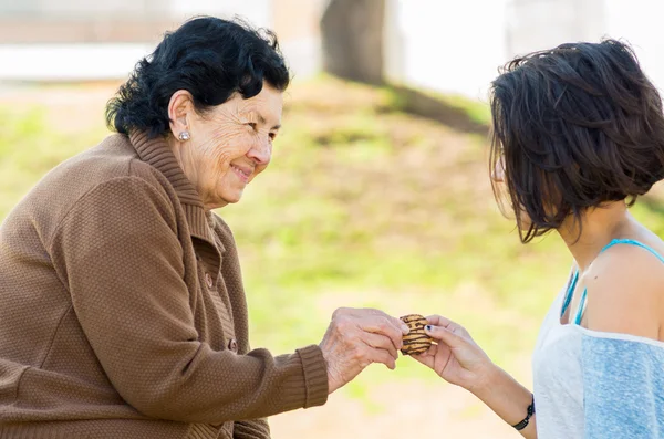 Schöne hispanische Großmutter und Enkelin genießen qualitativ hochwertige Zeit im Freien teilen Snacks — Stockfoto