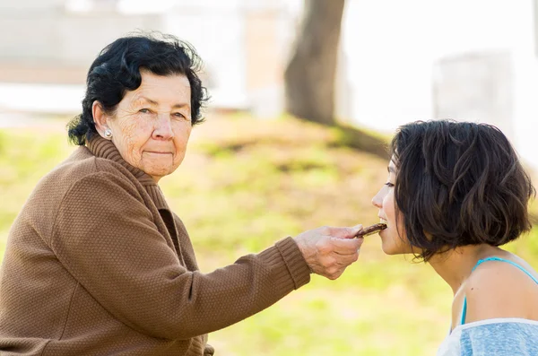 Lovely hispanic grandmother and granddaughter enjoying quality time outdoors sharing snacks — Stock Photo, Image