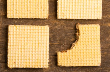 Closeup square cookies lined up on wooden surface with one of them missing a bite
