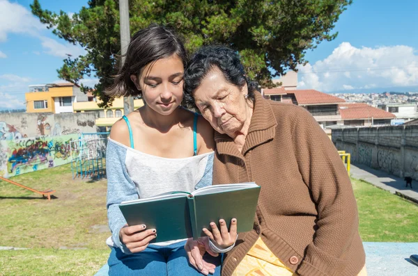 Lovely grandmother and granddaughter sitting together enjoying quality time outdoors reading in book — Stok fotoğraf
