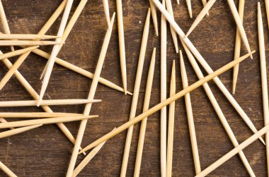 Many toothpicks lying in pile facing different directions on a dark wooden surface