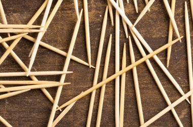 Many toothpicks lying in pile facing different directions on a dark wooden surface clipart