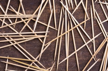 Many toothpicks lying in pile facing different directions on a dark wooden surface