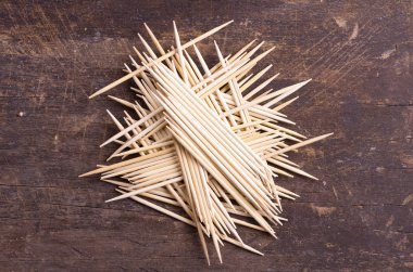 Many toothpicks tightly piled together facing different directions on dark wooden surface clipart