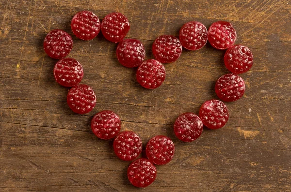 Lovely heart made out of raspberry hard candy on wooden surface — Stockfoto