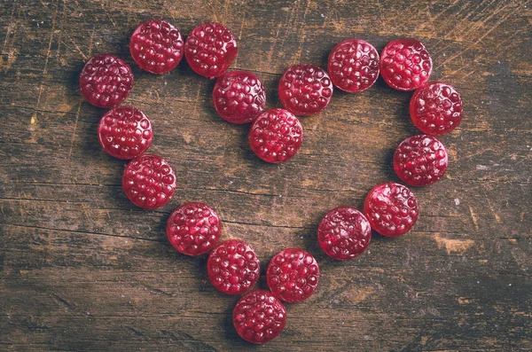 Lovely heart made out of raspberry hard candy on wooden surface — Stock fotografie