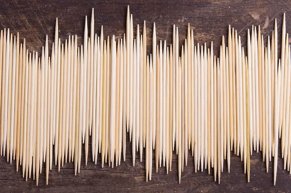 Big pile of toothpicks lying in an uneven horisontal line on dark wooden surface — 图库照片
