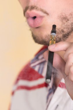 Closeup man with facial hair smoking on electronic cigarette, facing camera blowing smoke
