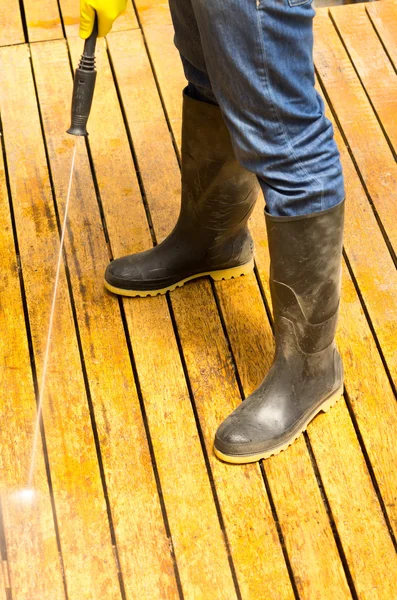 Man met rubberen laarzen met behulp van hoge waterdruk schoner op houten terras oppervlak — Stockfoto