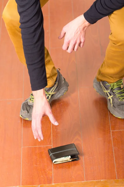 Man wearing beige jeans and dark sweater bending down to pick up wallet from ground — Zdjęcie stockowe