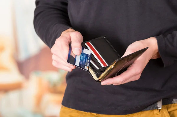 Man wearing beige jeans and dark sweater holding wallet open with both hands revealing its content to camera — Stockfoto