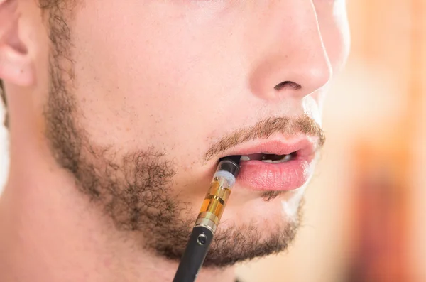 Closeup face of hispanic man with facial hair wearing dark sweater enjoying an electronic cigarette while posing for camera — ストック写真