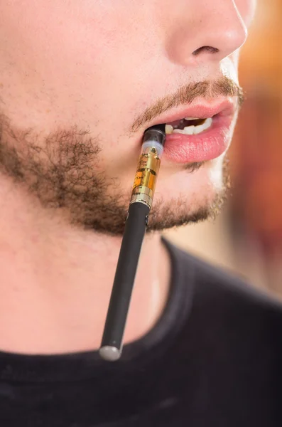 Closeup face of hispanic man with facial hair wearing dark sweater enjoying an electronic cigarette while posing for camera — Stok fotoğraf
