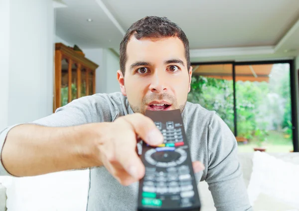 Closeup hispanic male wearing light blue sweater holding up remote control in front of camera, funny angle — 图库照片