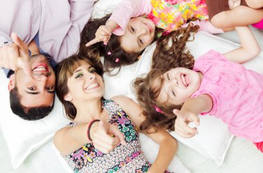 Adorable hispanic family lying down with heads touching showing facial expressions to camera, shot from above angle