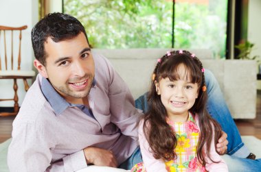 Proud hispanic father and adorable young girl posing together lying down, looking into camera smiling