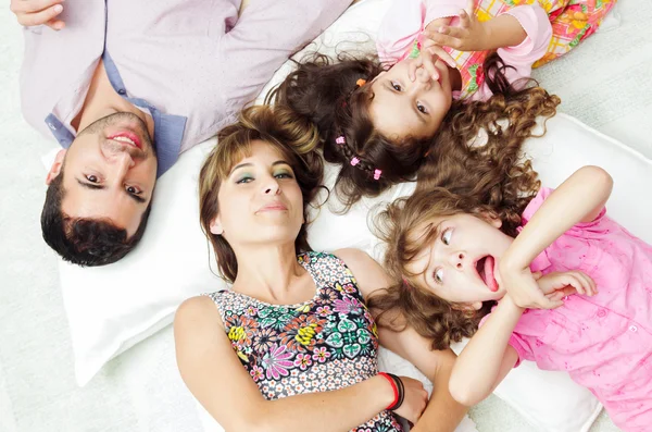 Adorable hispanic family lying down with heads touching showing facial expressions to camera, shot from above angle — Zdjęcie stockowe