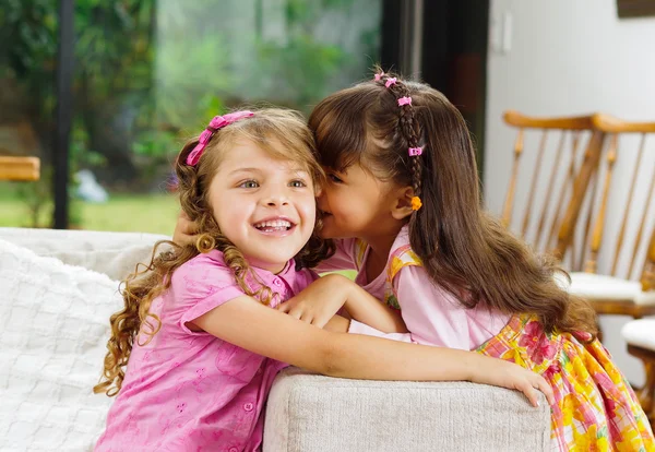 Brünette Kinderschwestern sitzen glücklich auf weißem Wohnzimmersofa und posieren mit typisch pinkfarbener Mädchenkleidung für die Kamera — Stockfoto