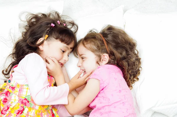 Young adorable hispanic sisters lying down playing and embracing each other happily while smiling to the camera, shot from above angle — Stock Photo, Image