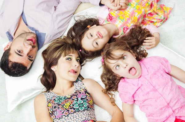 Adorable hispanic family lying down with heads touching showing facial expressions to camera, shot from above angle — Stockfoto