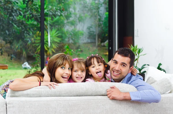 Beautiful hispanic family of four posing with heads sticking up from back sofa looking at camera smiling — Stock Photo, Image