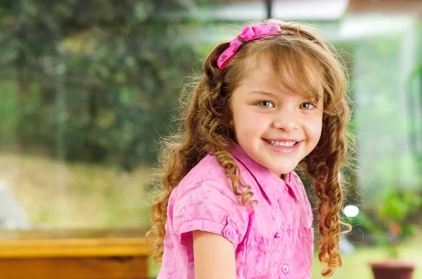 Beautiful young hispanic girl with pink clothing smiling cute at camera, blurry garden background — Stock Photo, Image