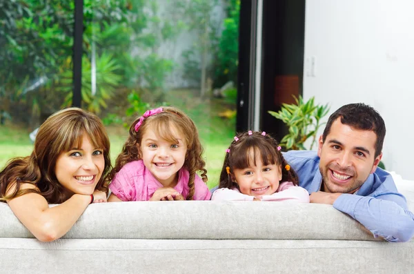 Bela família hispânica de quatro posando com cabeças levantadas do sofá traseiro olhando para a câmera sorrindo — Fotografia de Stock