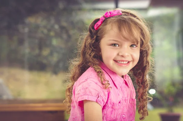 Entzückende brünette junge Mädchen in rosa Kleidung, die mit netten Lächeln in die Kamera schaut, Garten Hintergrund — Stockfoto
