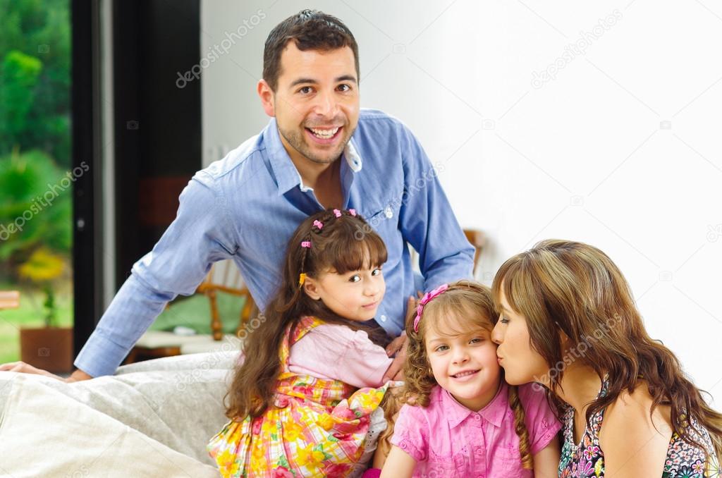 Beautiful hispanic family of four posing naturally while sitting in white sofa