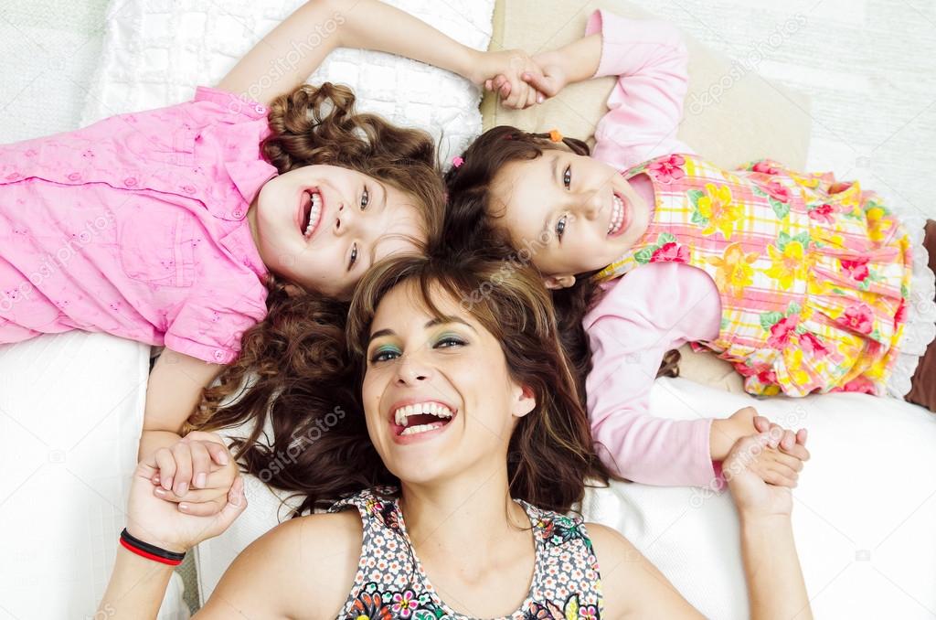 Young adorable hispanic sisters with mother lying down, heads touching and bodies spread out different directions closeup