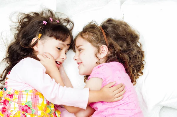 Young adorable hispanic sisters lying down playing and embracing each other happily while smiling to the camera, shot from above angle — Stock Photo, Image