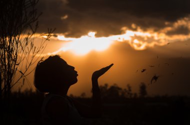 Teenage girl posing with sunset behind clouds in background creating spectacular colors, silhouette concept