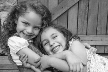 Adorable young brunette girls embracing hugging showing love and friendship, looking into camera black white edition