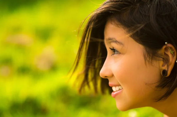 Headshot profile pretty teenage hispanic girl with half short hair and green blurry background — Stok fotoğraf