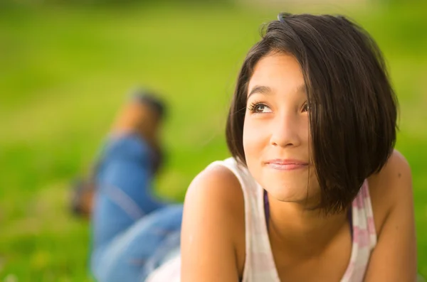 Pretty teenage hispanic girl wearing white top and shorts lying on grass relaxed facing camera — Stok fotoğraf