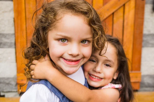 Adorable young brunette girls embracing hugging showing love and friendship, looking into camera — Stok fotoğraf