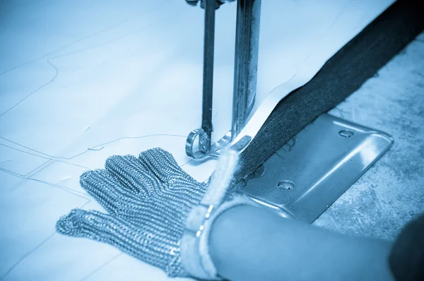 Mains portant des gants de protection utilisant une machine industrielle pour couper les tapis, textiles et autres tissus résistants — Photo